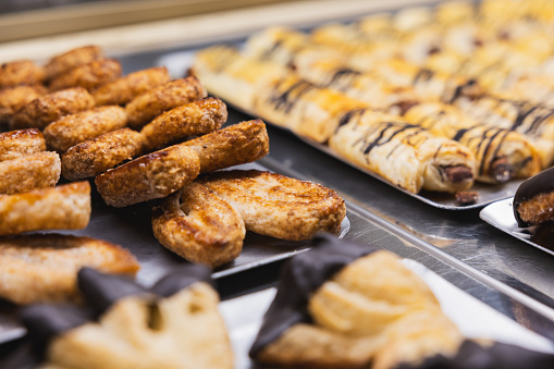 Variety of pastries on display in a bakery. The pastries are arranged on trays and are freshly baked.