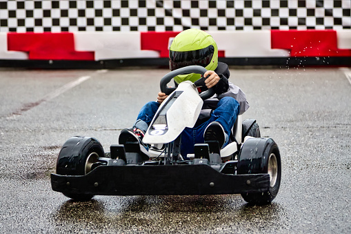 Young lover of extreme racing sports trains before a karting competition on the race track. Brave boy child racer in helmet driving children's electric karting