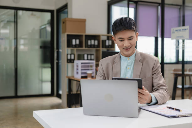 istock Businessman, manager, CEO, handsome Asian man, middle aged man sitting in office, working on paperwork, checking and reading documents, contracts and accounting reports with laptop. 1835351908