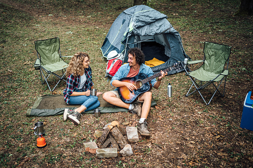 Young man playing the guitar to his girlfriend while they are camping