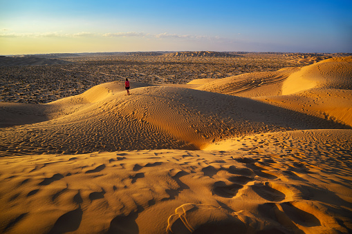 Woman watching sunset over the sand dunes of the Arabian Desert in Oman, near the city of Salalah.