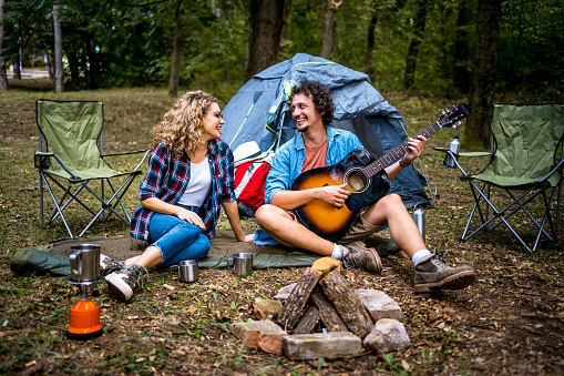Young man playing the guitar to his girlfriend while they are camping