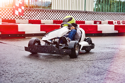 Brave boy child racer in helmet driving children's electric karting. Young lover of extreme racing sports trains before a karting competition on the race track.