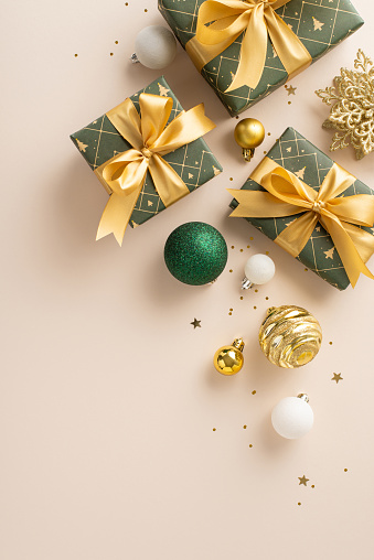 Lavishness and holiday inspiration captured. Top-view vertical photo of presents, luxurious baubles, snowflake ornament, gold sequins on light beige backdrop, providing open canvas for messages or ads