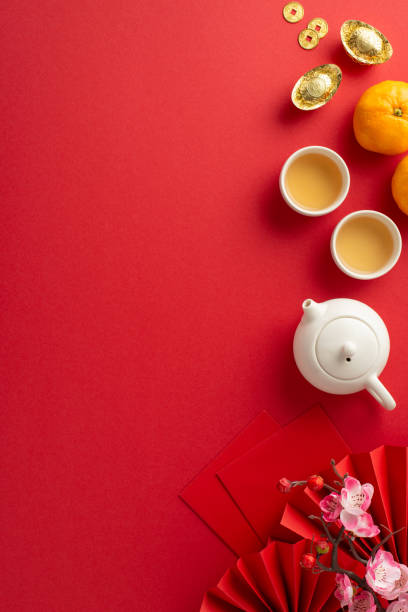 istock Dive into richness of Chinese New Year with sumptuous table setting. Overhead vertical shot of ornate fans, green tea accessories, Feng Shui symbols, citrus, sakura on red canvas, ready for your ad 1835395417