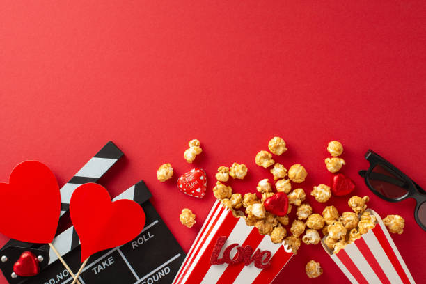 istock Love at First Frame: Top view of a clapperboard, 3D glasses, popcorn, chocolates, and heart decor on a red backdrop, signaling the launch of a romantic movie premiere 1835395421