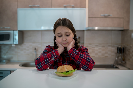 teen girl looking at appetizing Burger lying in front of her on the table