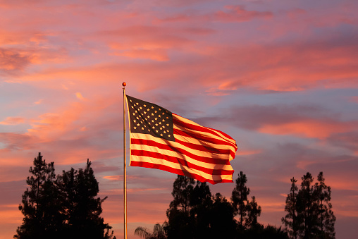 The American Flag stands in front of a orange an pink wispy sunset.