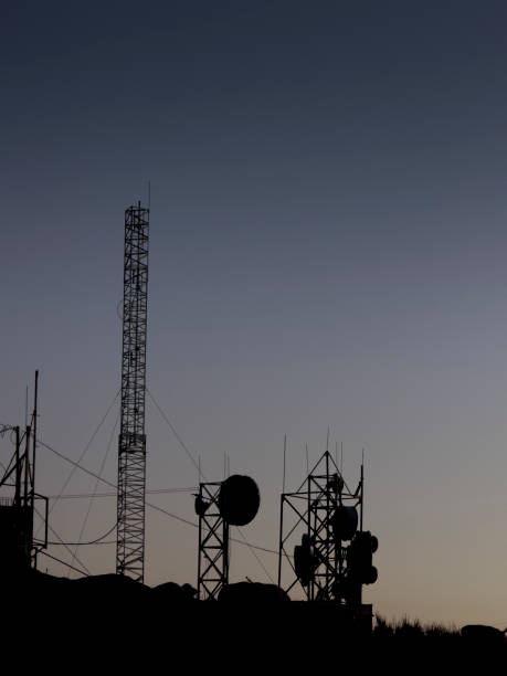 Against the backdrop of the setting sun's warm hues, a towering metal communication structure reveals its intricate silhouette, standing tall in the canvas of the sunset sky.