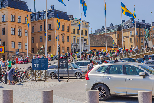 Sweden. Stockholm. 06.06.2023. Descending cobblestone street towards waterfront in central Stockholm, by royal castle, where people stroll amidst flags, celebrating Sweden's National Day.