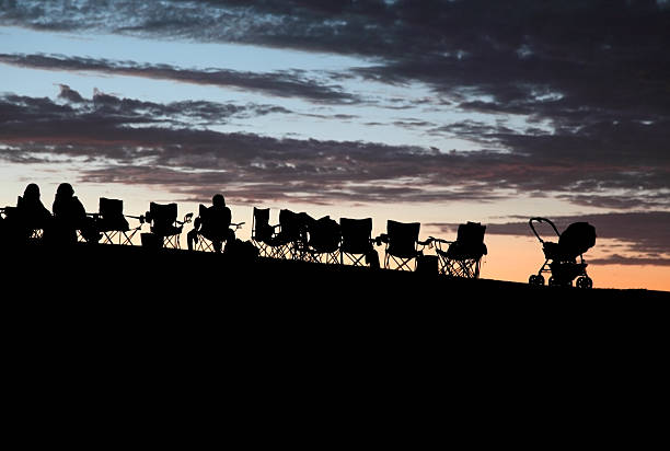 Silhouette of people sitting in a row of camping chairs on a hilltop looking at the fading sunset