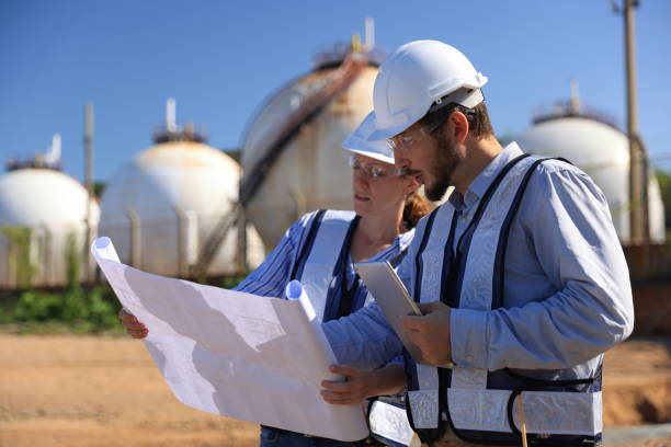 istock Male & Female engineer stand Discussing building plan at site, Engineers working outdoors against gas containers in the background 1835462101