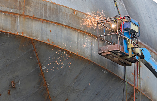 Man welding steel joints on ship under construction in shipbuilder's yard