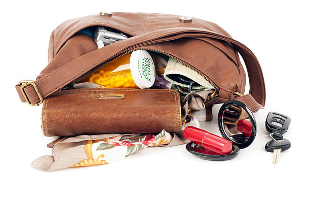 Purse: Open with Contents Spilling "Brown leather purse with contents spilling out, prescription medicine, a tube of lipstic on a mirror, and car keys. Studio isolated with light shadows.Please also see:" purse stock pictures, royalty-free photos & images