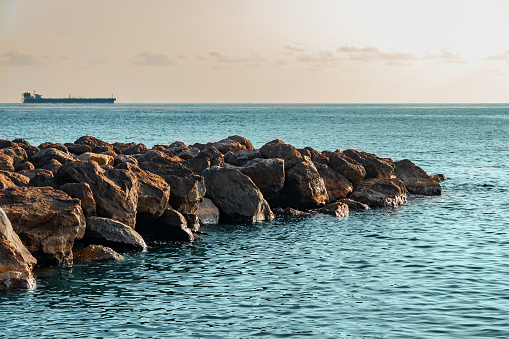 A beach with a breakwater made of large stone boulders. View of the sea breakwater made of stones. Seascape at sunset under a cloudy sky. Waves on the sea and dark clouds in the blue sky.