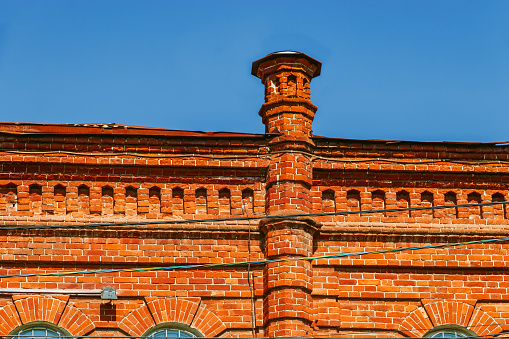 A fragment of the facade of an old red brick house. An old brick building with windows and a turret.