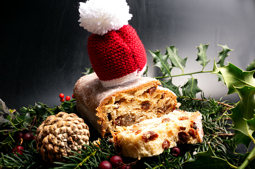 A heavenly delicious freshly baked snowy German Christmas Stollen with marzipan filling dressed up with a Santa's hat and surrounded by Christmas plants; its soft and moist, buttery and nutty texture infused with Christmas festive aroma of  rum, vanilla, cardamom, and cinnamon; which melts in your mouth for special breakfast on Christmas morning.