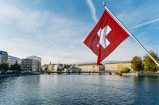 Flag of Switzerland over the lake in Geneva with the city in the background.