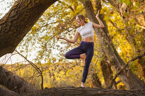 n the midst of autumn's charm, a woman finds equilibrium in a yoga balance position, surrounded by the golden hues of the season.