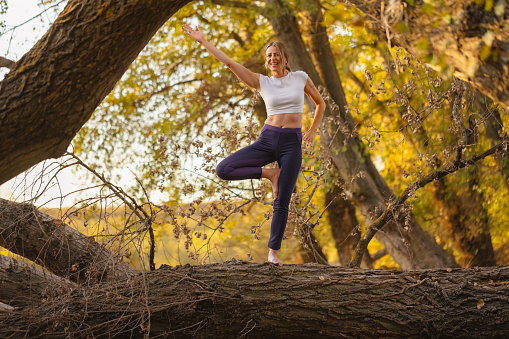 A moment of zen in nature as a female yoga instructor showcases her balance, merging with the serene beauty of the autumn scenery.