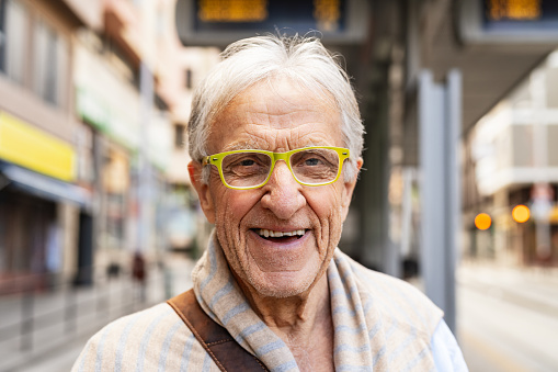 Happy senior man smiling in front of camera while waiting at tram station in the city