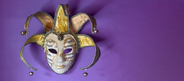 Front view of fancy golden Venetian carnival mask hanging on purple wall. Copy space for text.