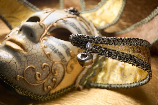 Close up of ball and details of golden Venetian mask, fancy carnival mask on golden surface.