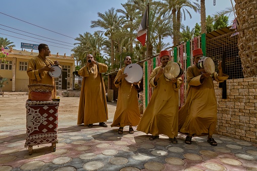 aswan, Egypt – September 26, 2023: A vibrant group of people in diversely colored outfits joyfully playing percussion instruments outdoors in the sunshine