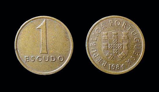 A closeup of Portugese Escudo coins on a black background