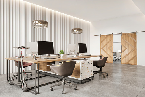 Open plan coworking interior with many desktop computers. Bright office with combination of terrazzo print, concrete floor, white paneled wall, pendant lamps, office chairs and barn sliding wooden door. Daylight render.