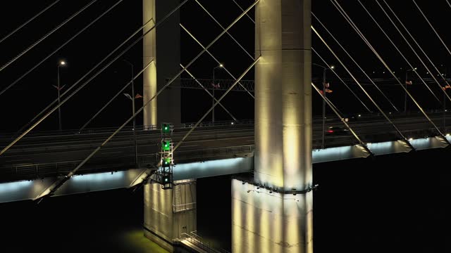 A cable-stayed highway bridge with tall concrete pylons illuminated by architectural lighting at night. Close-up of the massive base of the pylons