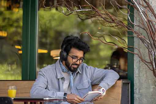 Leisure. Dark-haired young hindu man in headphones with a book in hands
