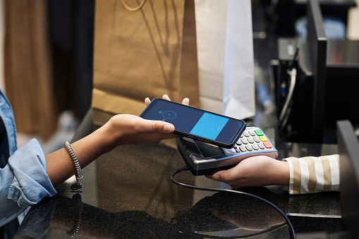 Closeup of unrecognizable female customer paying with her smartphone at clothing store