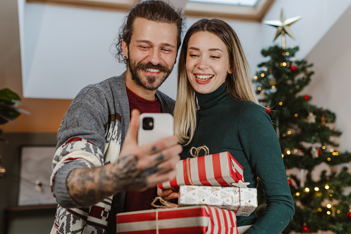 Happy young couple spending time at home during the winter holidays. A young man is holding smart phone