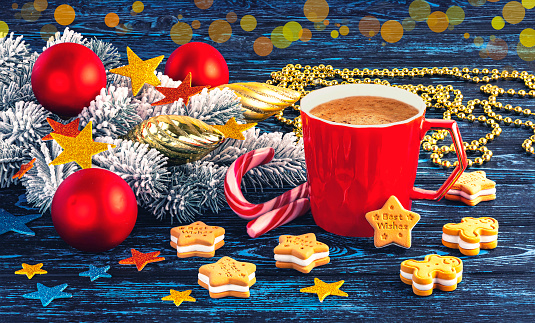 Red cup of coffee, gingerbread and snowy branch of Christmas tree with Christmas decorations. Festive Christmas composition on a blue wooden background