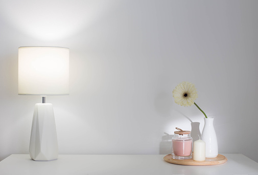 gerber in vase, candles and modern lamp on white shelf