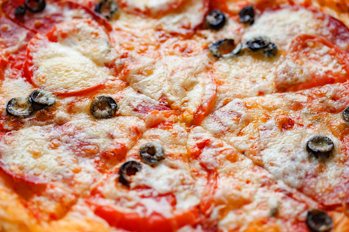 Pizza with cheese, salami and black olives, close-up, selective focus, cut