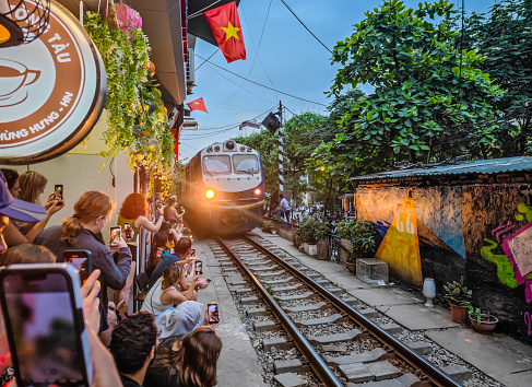 Hanoi, Vietnam - 04 30 2023: Train passing by people in Hanoi train street in Vietnam. A narrow street of the Hanoi Old Quarter