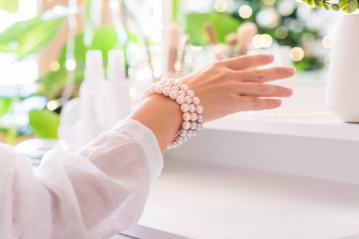 Woman puts on jewelry, pearl bracelets on the hand and  sitting near dressing table with make up accessories.