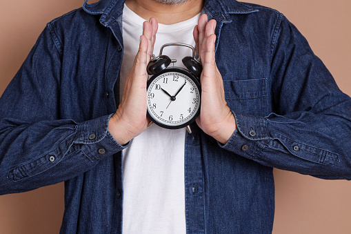 Hand of asian man is holding a clock on blue background, Time management, Balance