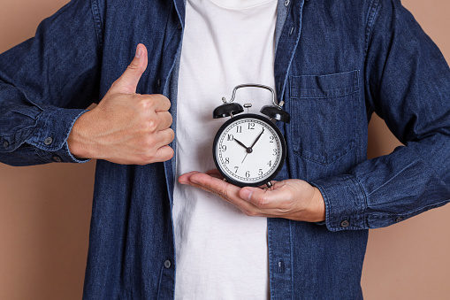 Hand of asian man is holding a clock on blue background, Time management, Balance