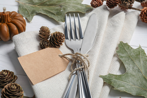 Thanksgiving day table setting. Cutlery, napkin and autumn decoration on white wooden background, closeup