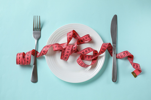 Plate, cutlery and measuring tape on light blue background, flat lay. Diet concept