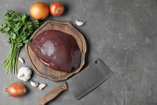 Piece of raw beef liver, knife and products on grey table, flat lay. Space for text