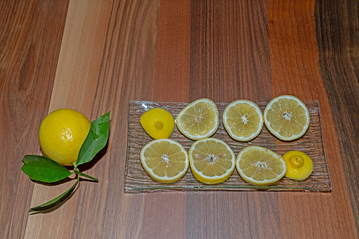 Sliced lemons on a glass plate with a green leafy lemon.
