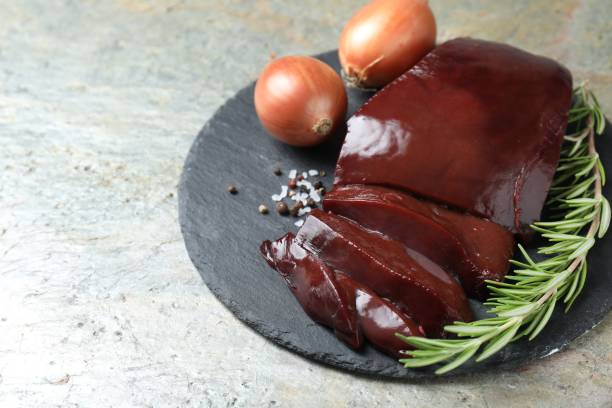 Cut raw beef liver with rosemary and onions on grey table, closeup. Space for text