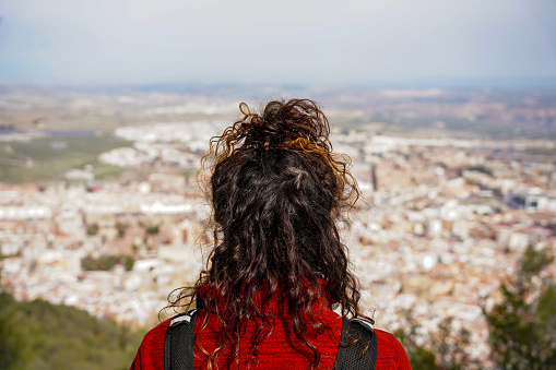 Rear view of a young woman gazing the landscape from the top of a hill