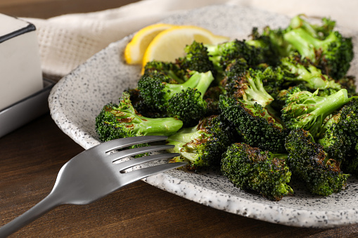 Tasty fried broccoli and fork on wooden table, closeup
