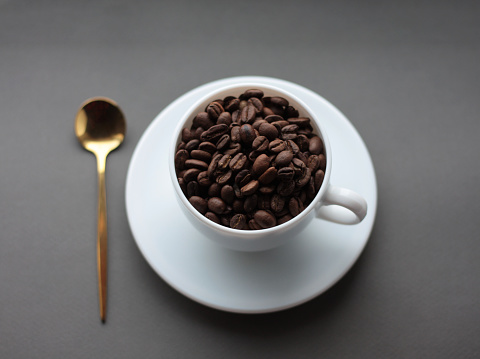 cup of coffee with coffee beans on a saucer with gold spoon