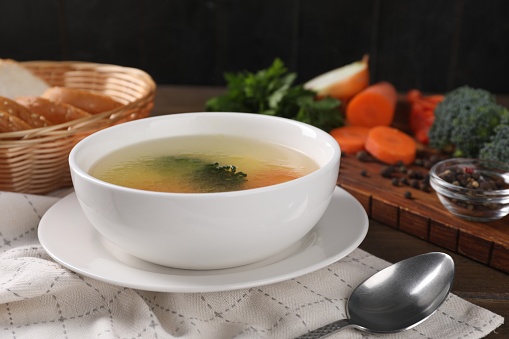 Tasty soup with vegetables in bowl served on wooden table, closeup